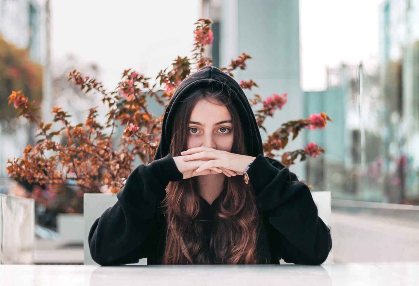woman in hoodie with hands in front of face
